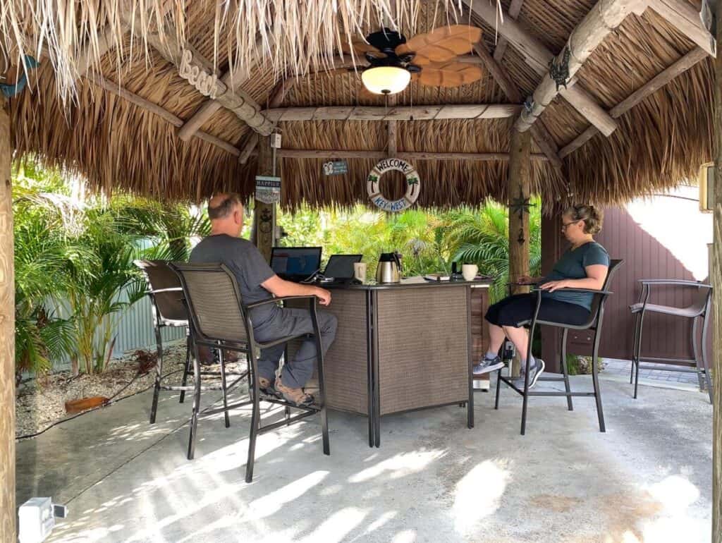 Image of a couple at work on laptops in a tiki hut style shelter
